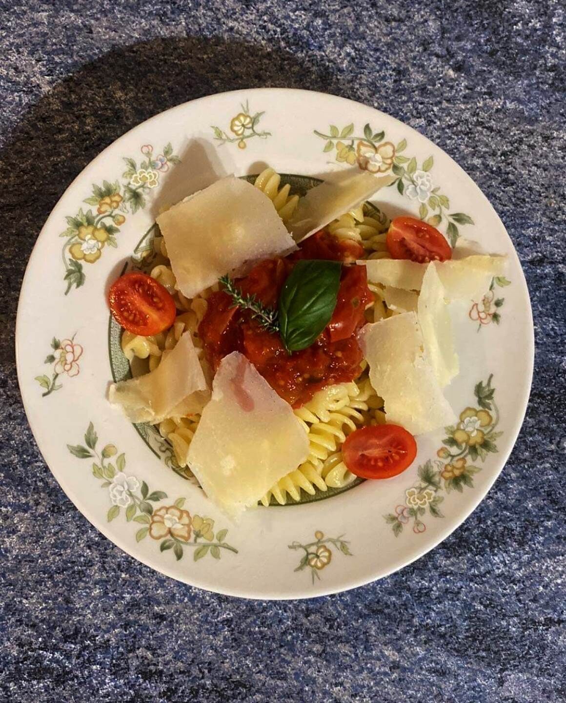 A plate of pasta with tomato sauce, cheese, and basil on a floral-patterned plate.