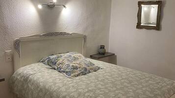 Une chambre à coucher comprenant un lit, une table de chevet, un miroir fixé au mur et un luminaire au plafond.