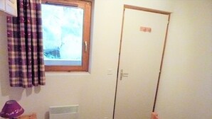 Une petite pièce avec un lit, une fenêtre avec des rideaux, un radiateur et une porte.