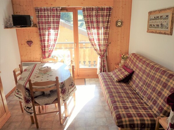 Um quarto acolhedor com decoração em madeira, uma mesa de jantar com cadeiras, um sofá e uma televisão em uma prateleira.
