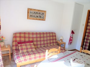 Una habitación acogedora con un sofá de cuadros, una silla de madera, una mesita con una lámpara y un cuadro colgado en la pared.