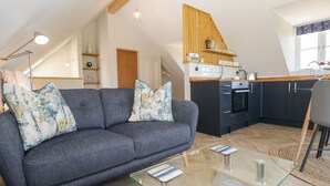 Eine moderne Loft-Wohnung mit grauem Sofa, einem Glastisch, einer Küche mit dunklen Schränken und einem Holzbalken an der Decke.