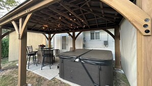 A covered patio with a hot tub, outdoor seating, and a wooden pergola structure. - NEW! Updated *|* Stylish *|* OP getaway w/ Hot Tub (Overland Park)
