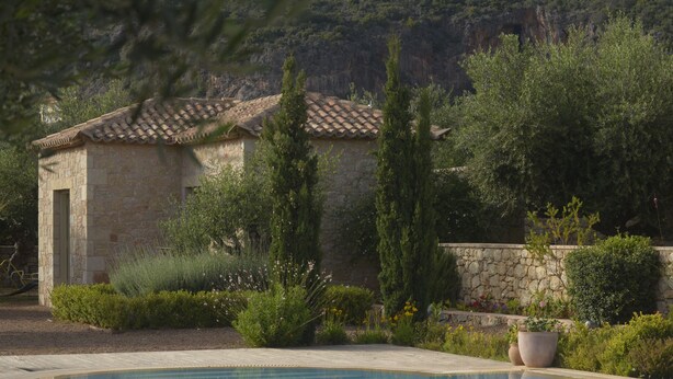 A stone building with a tiled roof, surrounded by lush greenery and a swimming pool. - Liodentra (West Mani)