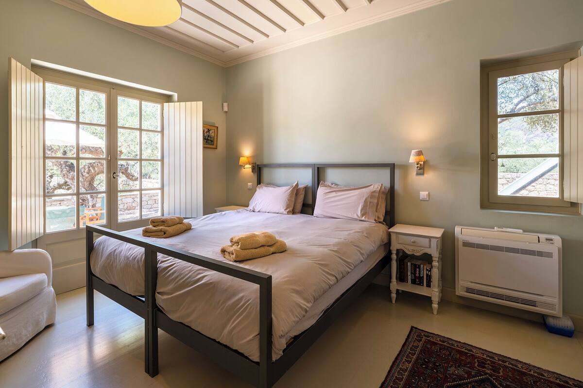 A bedroom with a bed, bedside lamps, a radiator, and a view of the outdoors.