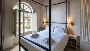 A bedroom with a four-poster bed, a bedside table with a lamp, and a window with curtains. - Liodentra (West Mani)