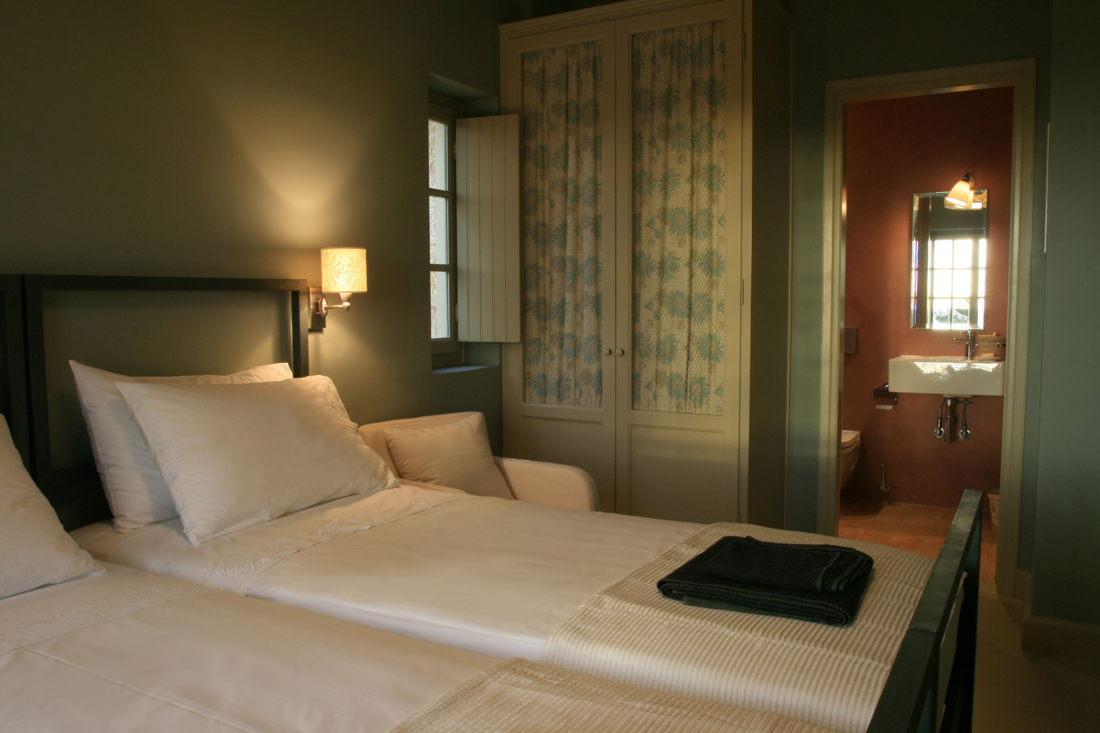 A neatly made bed with pillows, a bedside lamp, and a folded towel on the bed.