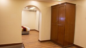 A room with a wooden wardrobe, a bed with a red and white blanket, and a wooden floor.