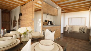 Un coin repas avec un plafond en bois, une cuisine à l’arrière-plan et un canapé dans l’espace salon.