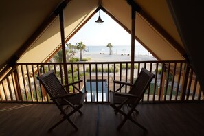 Ein Balkon mit Holzkufen und einem Tisch, mit Blick auf einen Strand mit Palmen und einem wolkenlosen Himmel.