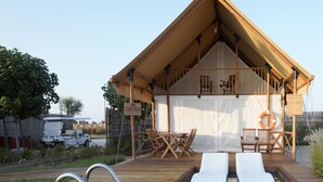 Un espace piscine comprenant deux chaises longues, une terrasse en bois et un coin salon couvert avec vue sur l’eau.