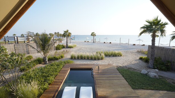 Une terrasse en bois avec un jacuzzi et des chaises longues donnant sur une plage.