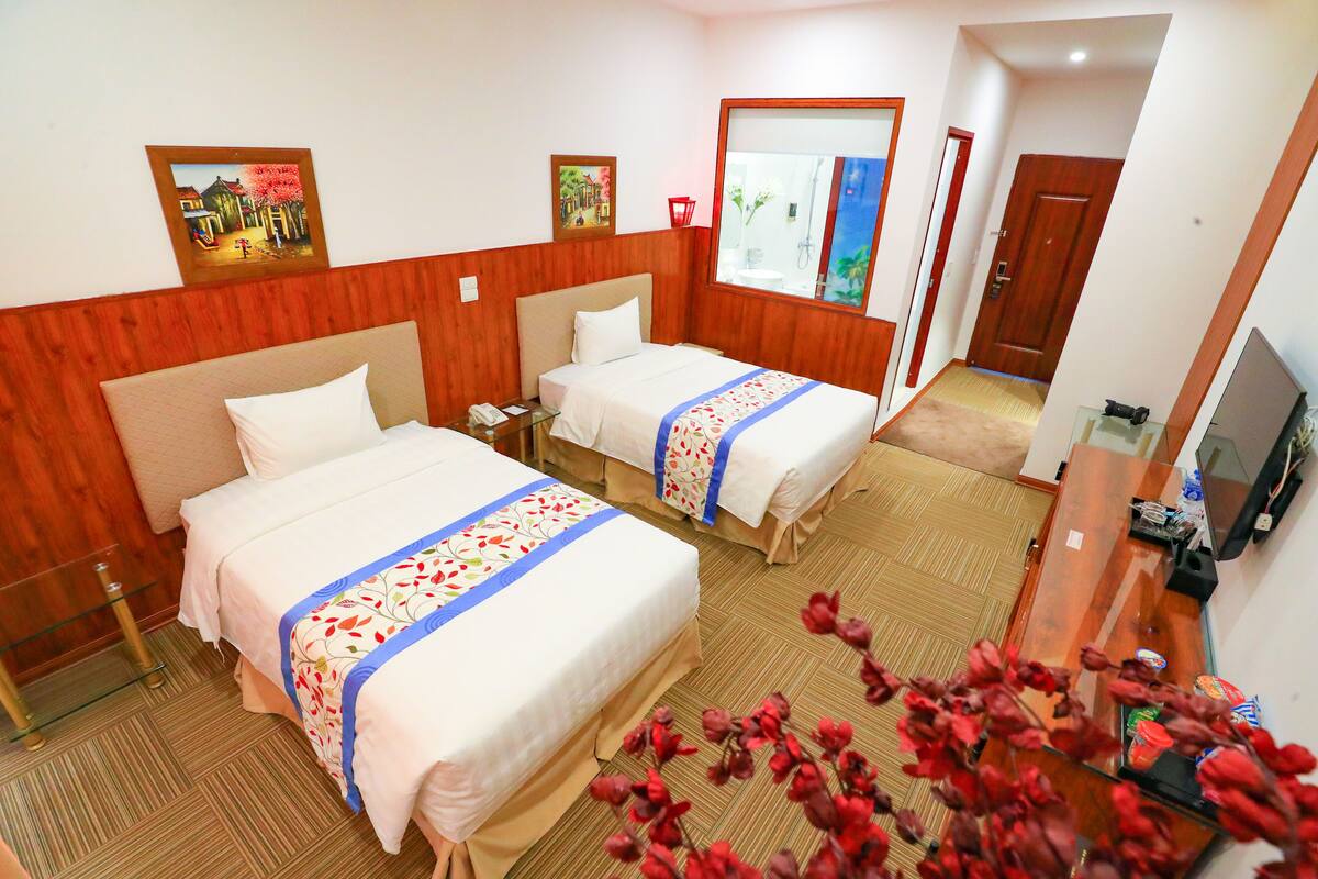 Habitación de hotel con dos camas, paneles de madera, un televisor y un espejo.