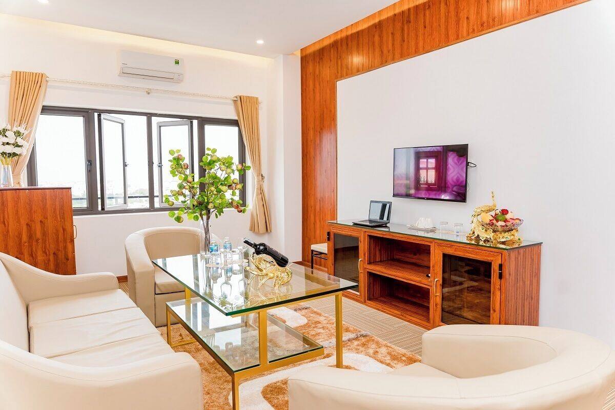 Una sala de estar moderna con una mesa de centro de vidrio, sofás blancos, un aparador de madera y un televisor en la pared.