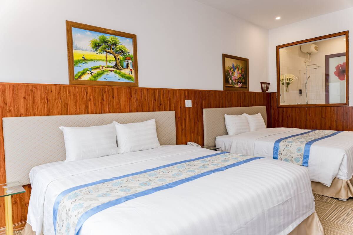 Habitación de hotel con dos camas, cabecero de madera y un cuadro de un paisaje.