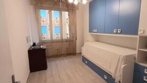 Un dormitorio con una cama, un tocador, un ventanal con cortinas y un candelabro.