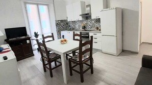 Cocina compacta con armarios blancos, un refrigerador blanco y una mesa de comedor con sillas.