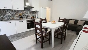 Una cocina moderna con armarios blancos, un salpicadero de azulejos y un comedor con mesa blanca y sillas oscuras.