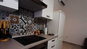 Una cocina compacta con armarios blancos, una campana extractora de acero inoxidable, horno empotrado y refrigerador.