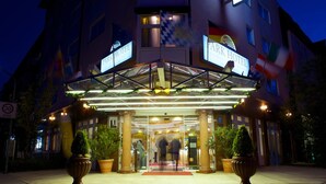 A hotel entrance with a glass canopy, potted plants, and a red carpet. - Park Hotel Laim Serviced Apartments (Munich)