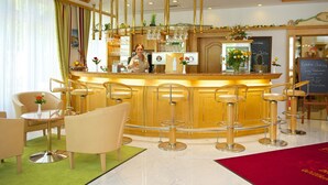 A bar area with a counter, bar stools, and a seating area with chairs and a table. - Park Hotel Laim Serviced Apartments (Munich)