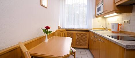 Una cocina compacta con armarios de madera, un microondas, una tetera y una pequeña mesa de comedor con sillas.