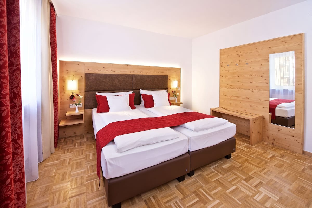 A modern hotel room with a large bed, wooden headboard, bedside tables, and a mirror.