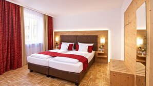 A double bed with a wooden headboard, red curtains, and a wooden bench. - Park Hotel Laim Serviced Apartments (Munich)