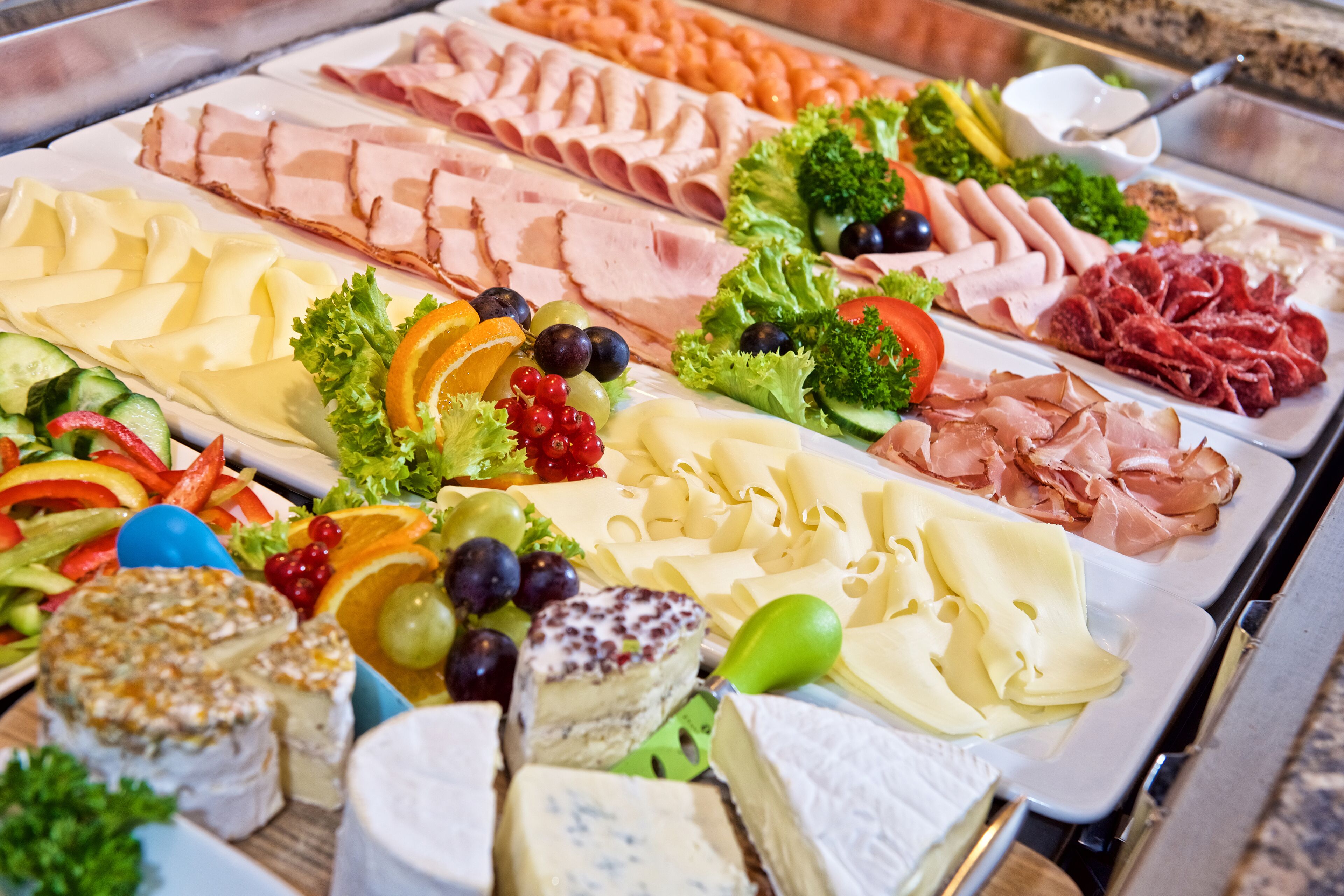 A buffet with various cheeses, meats, and fruits.