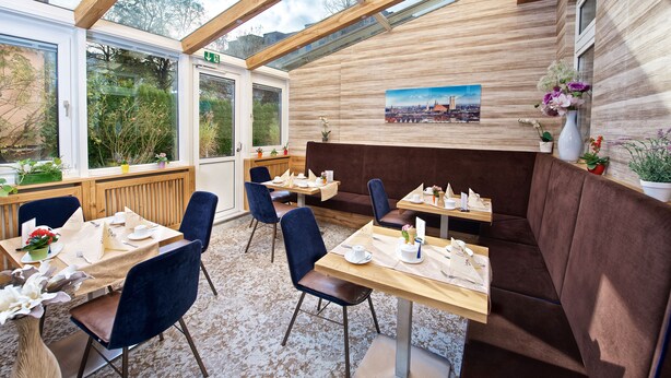 A restaurant with wooden tables, blue chairs, and a wooden wall with a cityscape painting. - Park Hotel Laim Serviced Apartments (Munich)