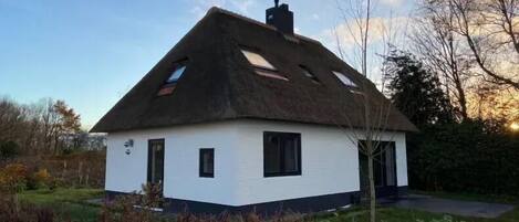 A white house with a thatched roof, multiple windows, and a chimney.