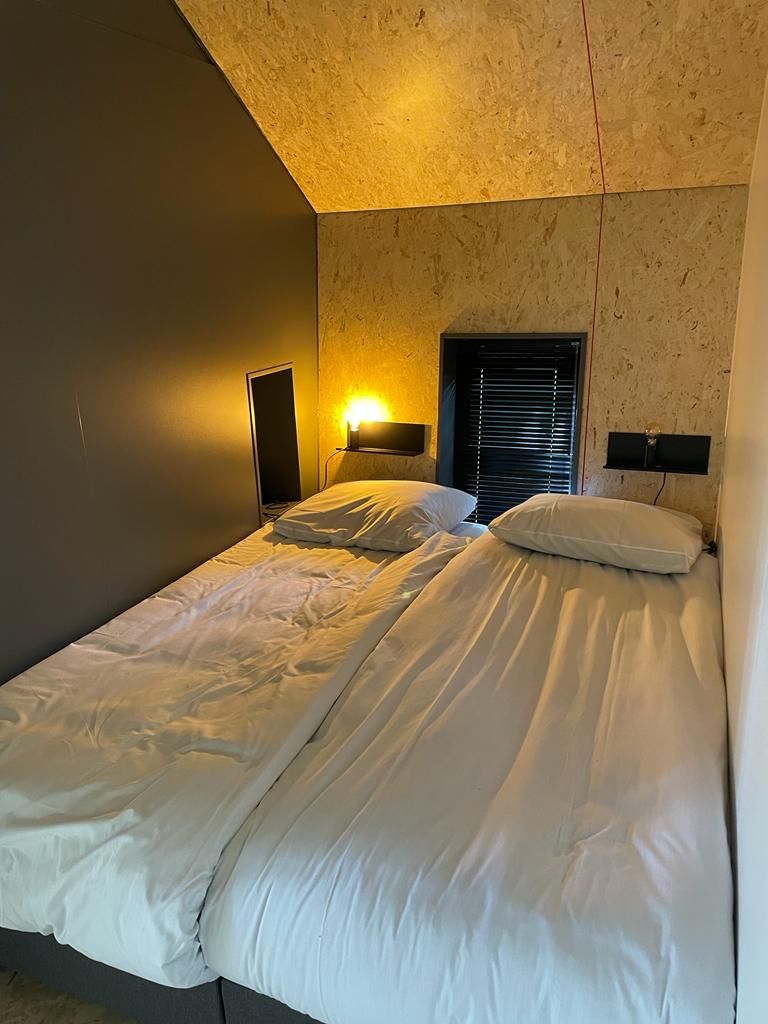 A double bed with white linens in a room with a textured wall and a slanted ceiling.