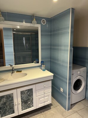 Une salle de bain avec un grand miroir, un lavabo, un lave-linge et des placards.