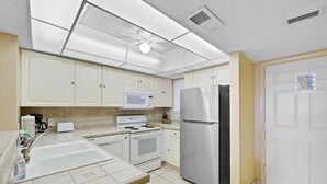 Una cocina con armarios blancos, un refrigerador de acero inoxidable, un microondas, una estufa y un ventilador de techo.