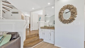 Un intérieur moderne avec un escalier menant à un deuxième étage, un coin cuisine doté de meubles blancs et un miroir décoratif accroché au mur.