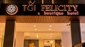 La entrada al hotel boutique TGI FELICITY, con un diseño moderno, presenta un frente de vidrio y una puerta de metal.