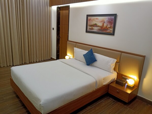 A hotel room with a large bed, wooden headboard, two bedside tables with lamps, a painting on the wall, and a window with curtains.
