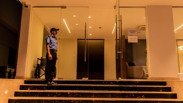 Una persona está de pie sobre escalones de mármol en un vestíbulo moderno con puertas de vidrio y una silla de ruedas.