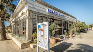 Restaurante PSAROLIMO con una pizarra de menú, mesas al aire libre y plantas en macetas.