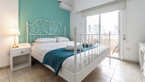 Un dormitorio con cama, mesita de noche, lámpara y vistas al exterior.