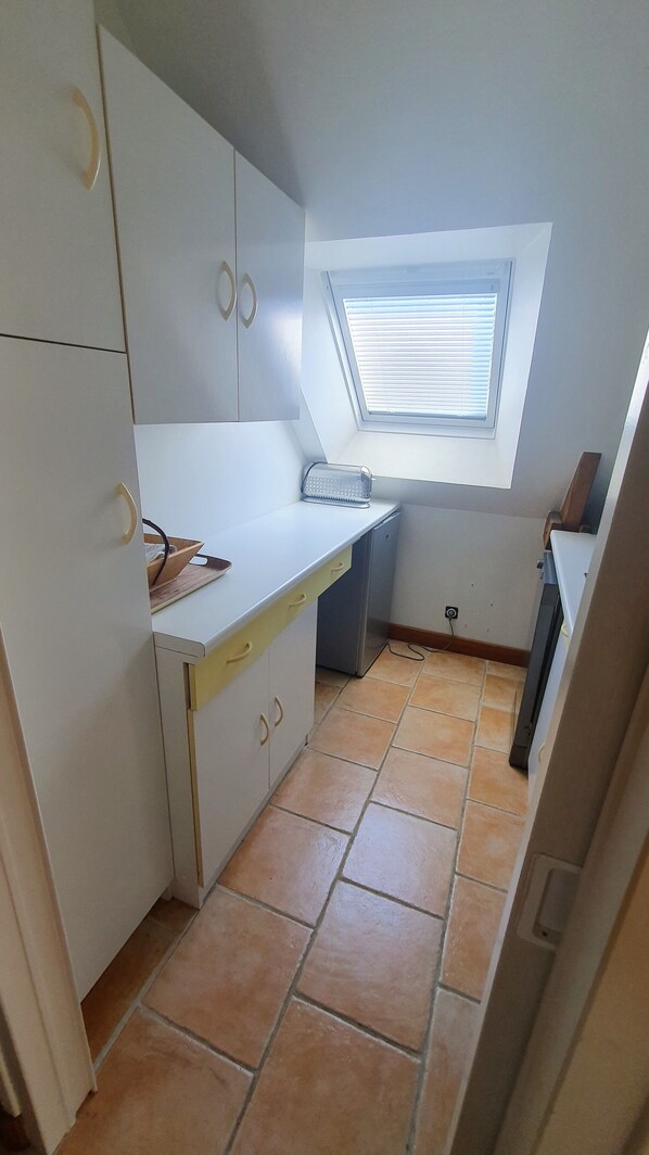 A compact kitchen with white cabinets, a small countertop, and a window above the sink.