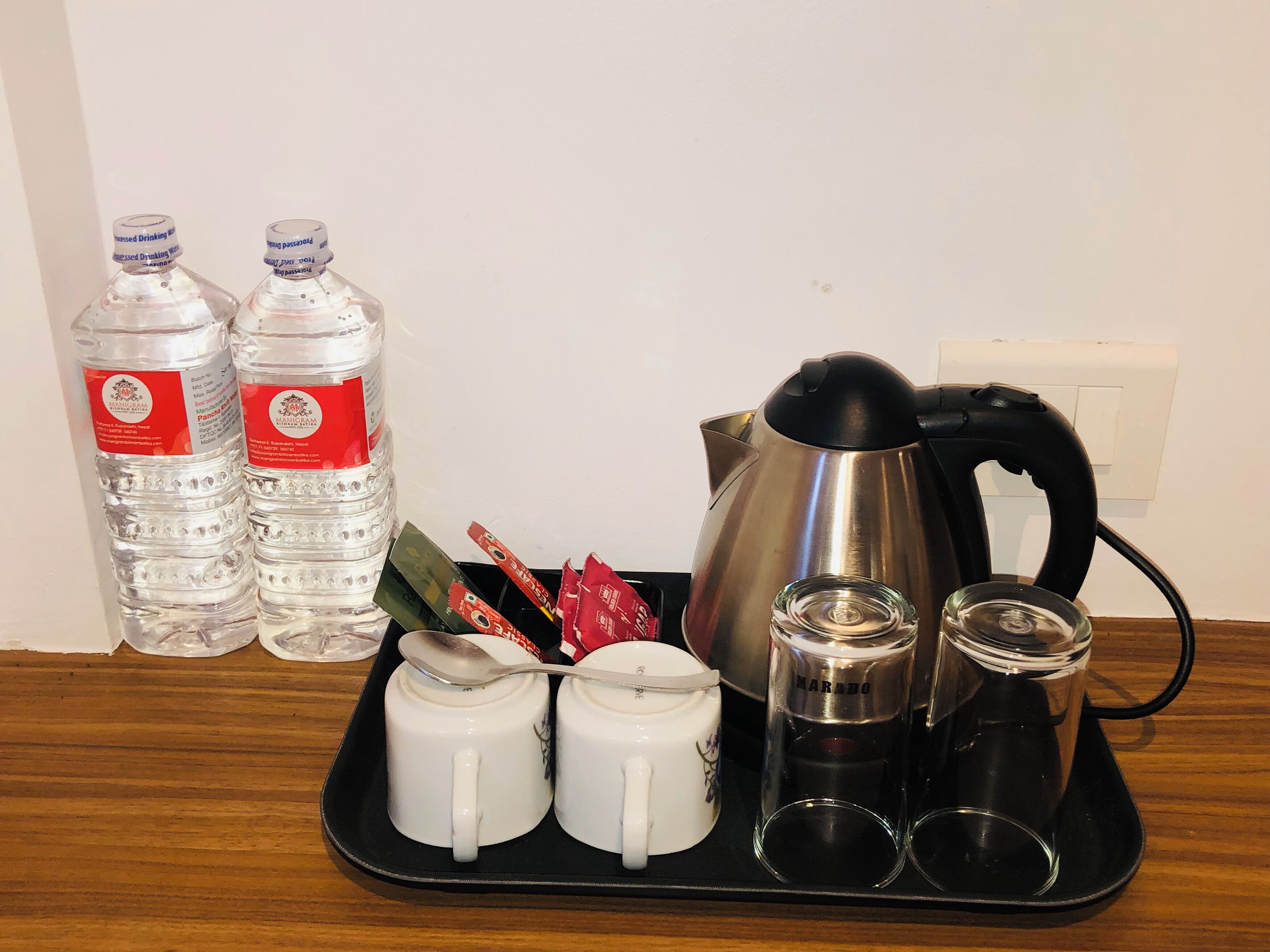 A tray with a kettle, two cups, two shot glasses, and two bottles of water.