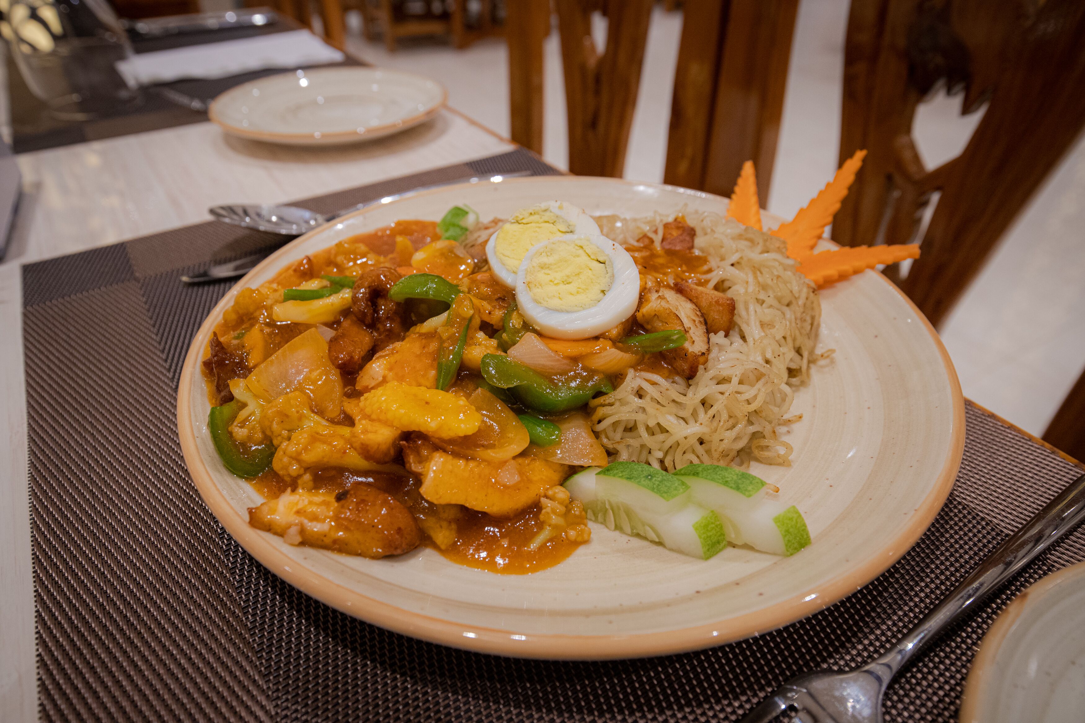 A plate of food with noodles, vegetables, and a boiled egg on a placemat.