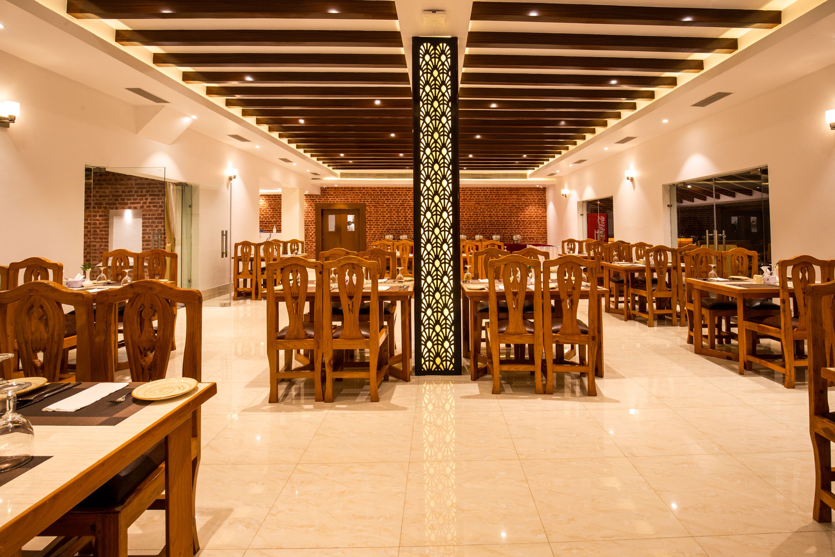 A spacious restaurant with wooden tables and chairs, a central decorative pillar, and brick walls.