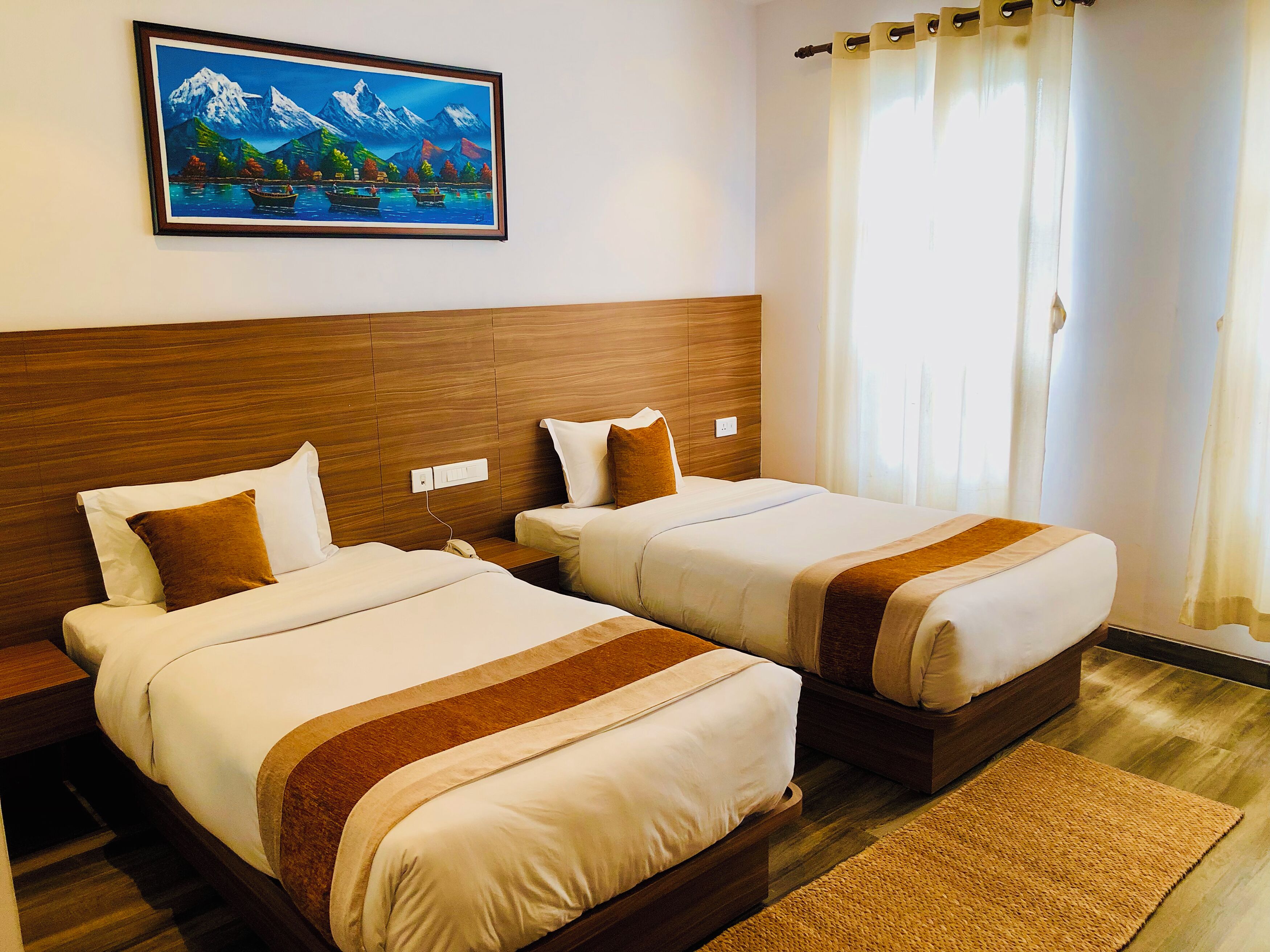 Habitación de hotel con dos camas, cabecero de madera, un cuadro de un paisaje montañoso y una ventana con cortinas.