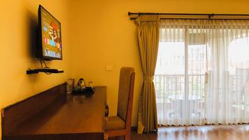 A living room with a wooden coffee table, a television mounted on the wall, a chair, and a window with curtains.
