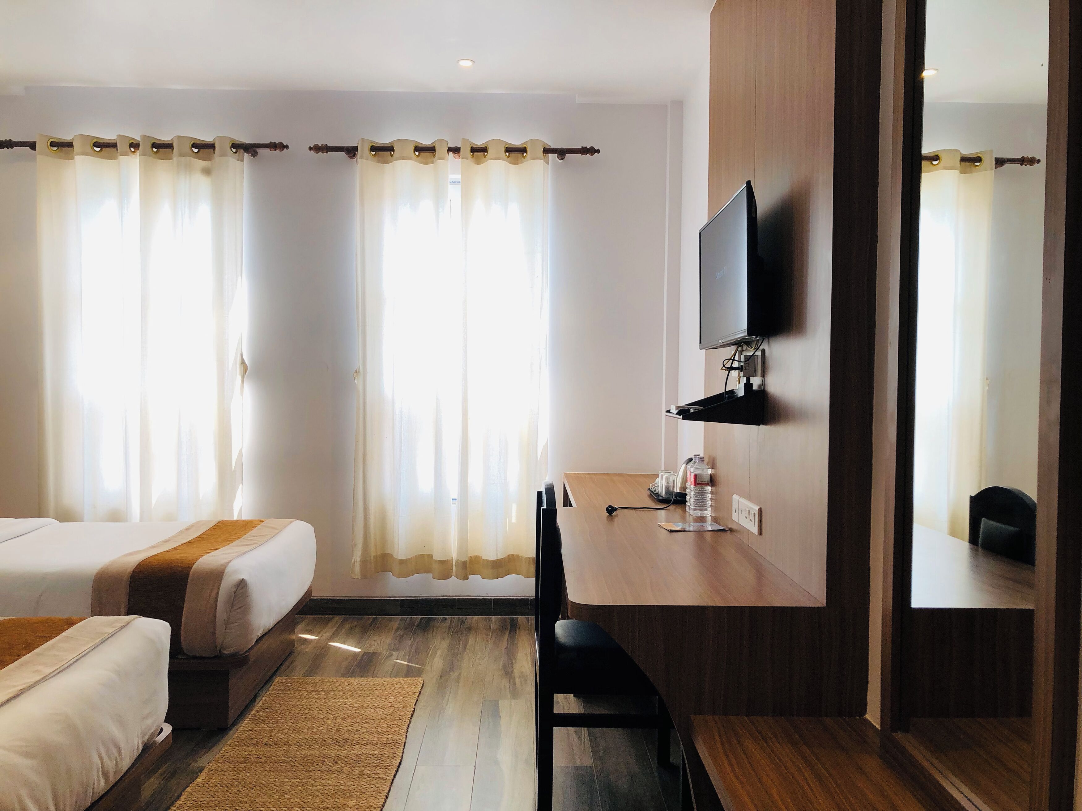 A hotel room with two beds, a desk with a chair, a TV mounted on the wall, and a large mirror.