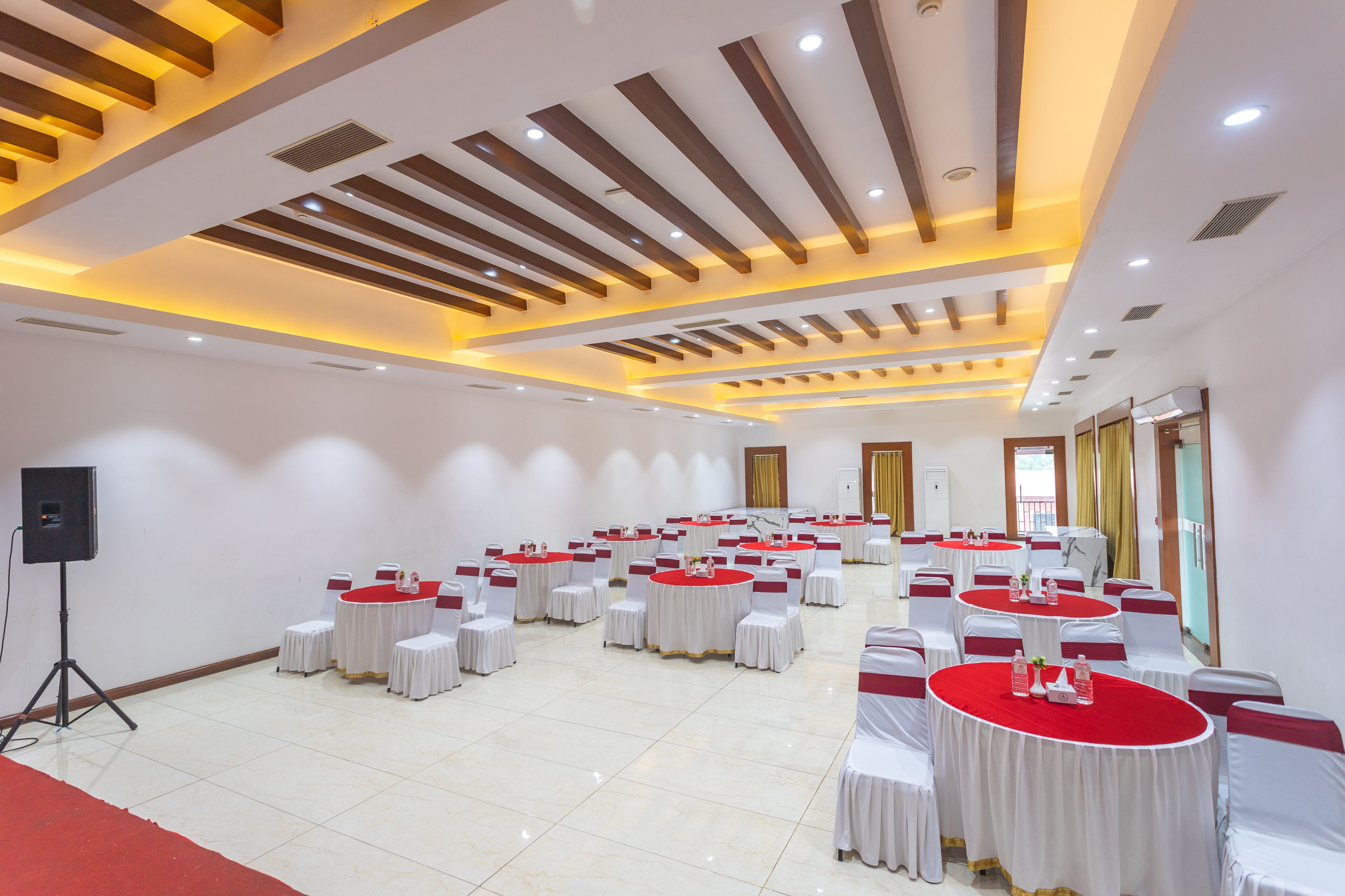 A conference room with round tables, white chairs, and a red carpet.