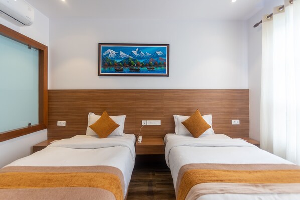 Habitación de hotel con dos camas, un cabecero de madera, un cuadro de montañas y barcos, y una ventana con cortinas.