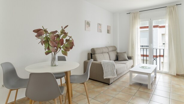 Una sala de estar moderna con una mesa de comedor, sillas grises, un sofá y una pequeña mesa blanca.